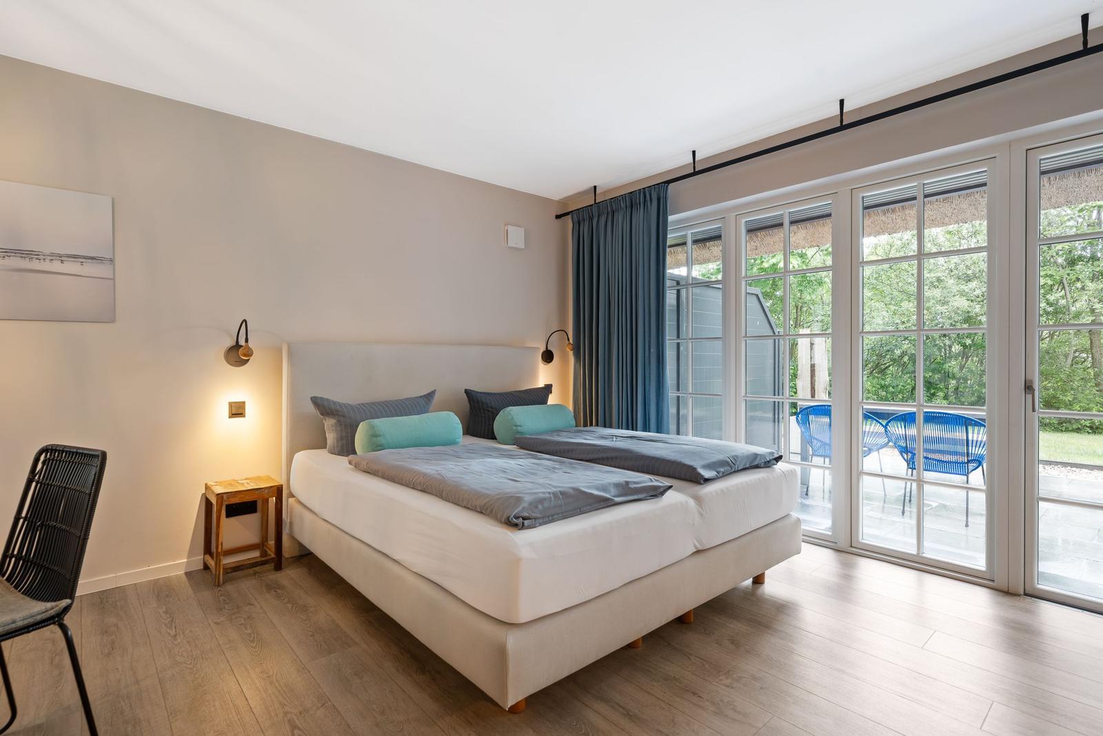 Schlafzimmer mit Doppelbett, Holzboden und großem Fenster zur Terrasse.