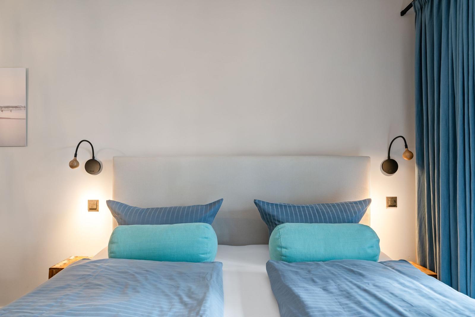 Zwei Betten mit blauen Kissen und Vorhängen an der Wand.