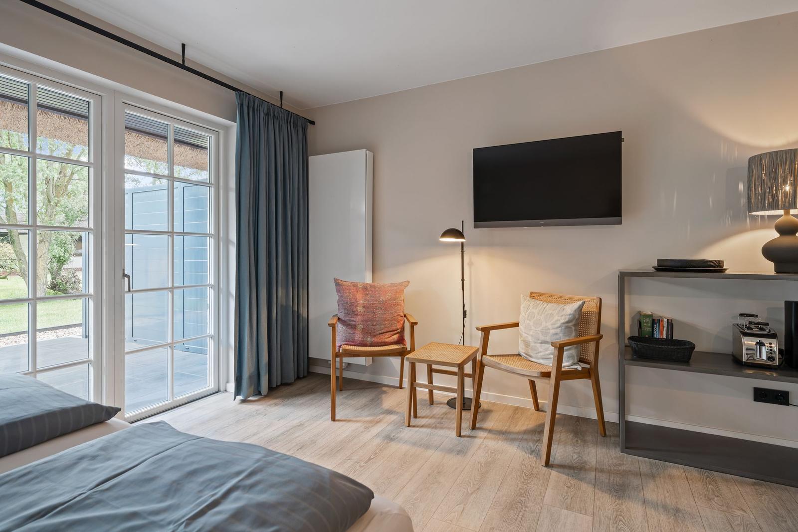 Zimmer mit Bett, zwei Stühlen, Fernseher und Blick auf Balkon.