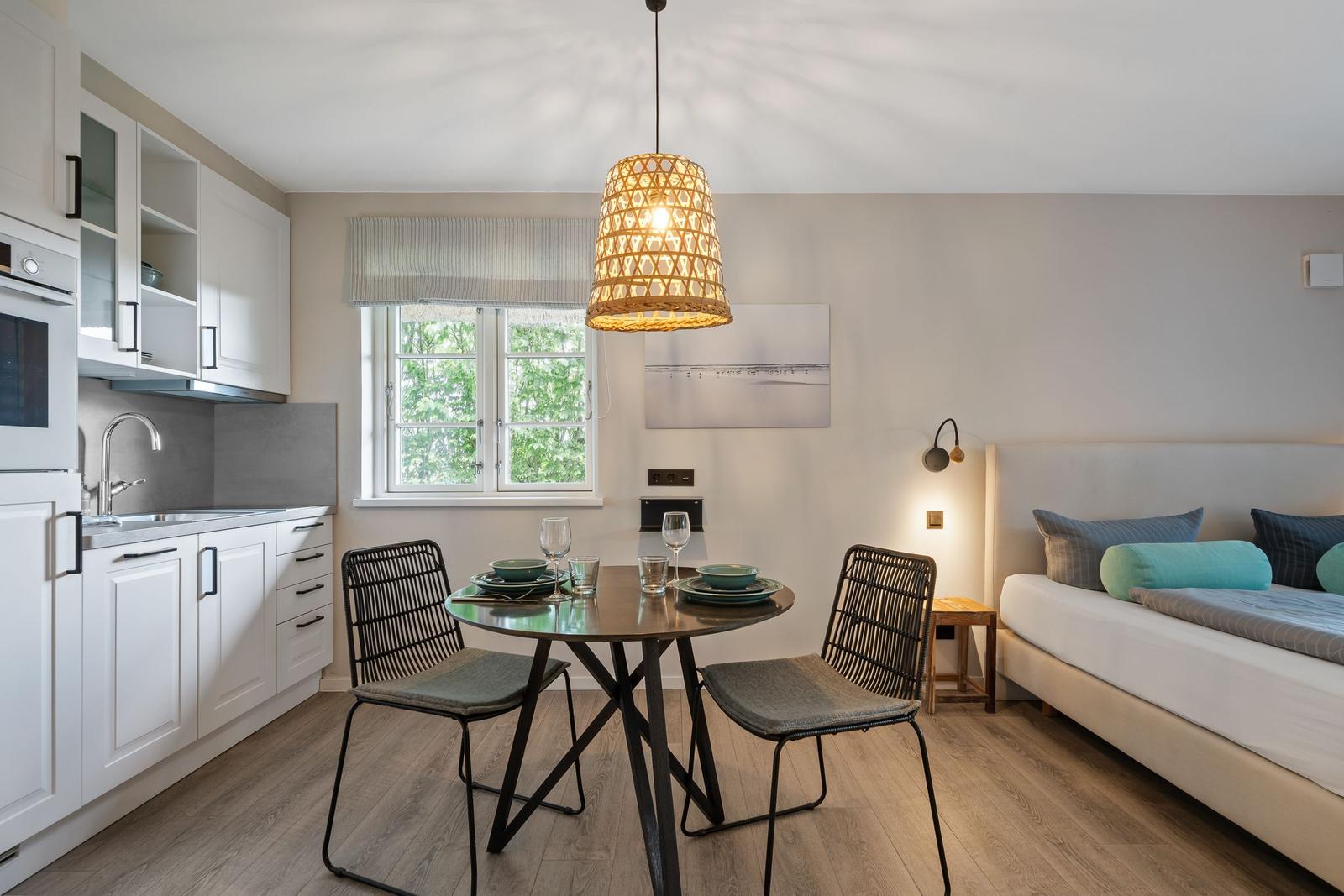 Küche, Essbereich und Schlafzimmer in einem hellen Raum mit Holzboden und Fenster.