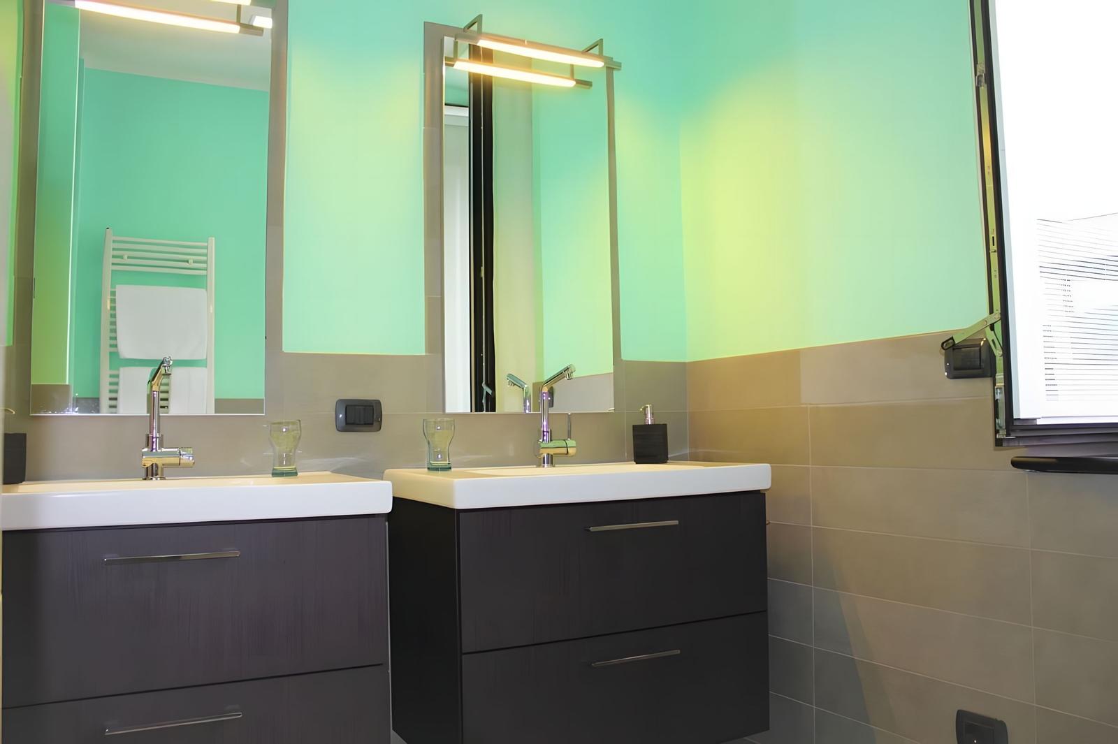 Two sinks with mirrors and lighting on green-toned walls.