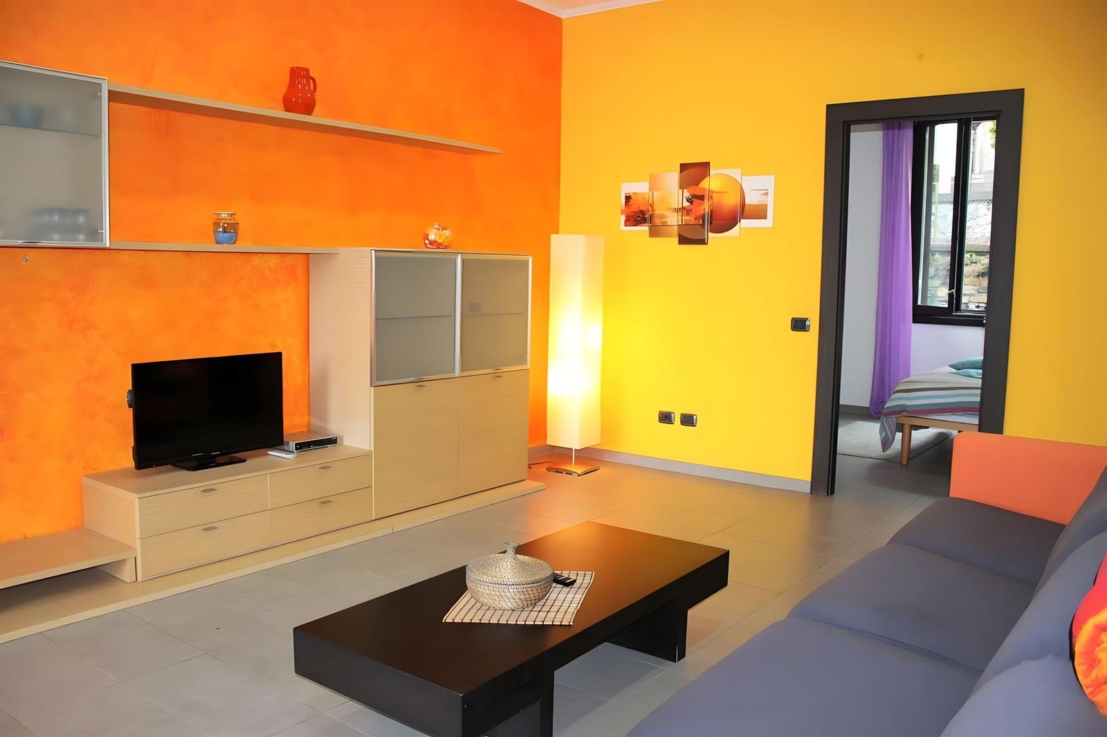 Living room with orange-yellow walls, sofa, coffee table, and TV.