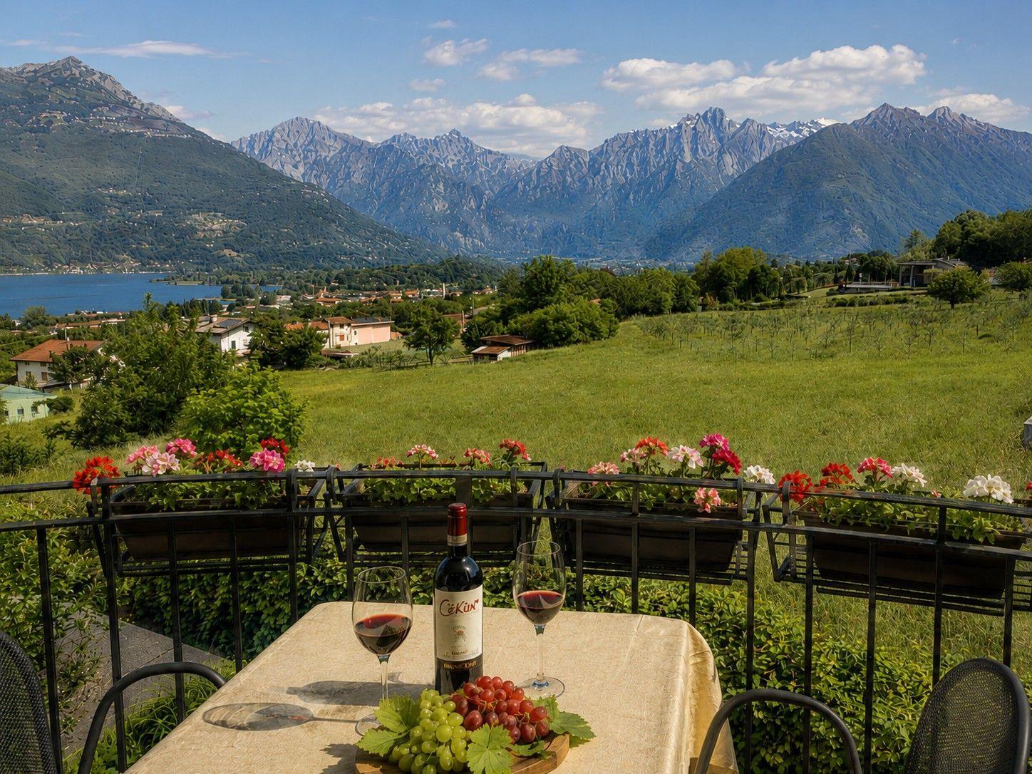 Tisch mit Wein und Trauben auf Balkon mit Blick auf See und Berge.