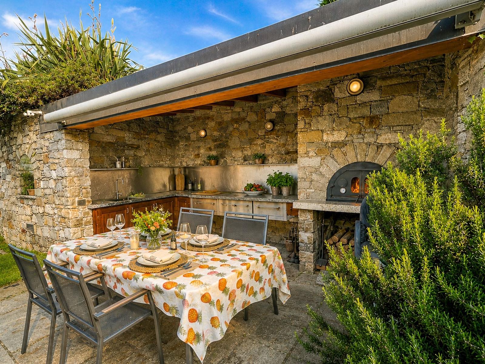 Außenküche mit Steinmauer, Grill und gedecktem Tisch mit Obstschale.