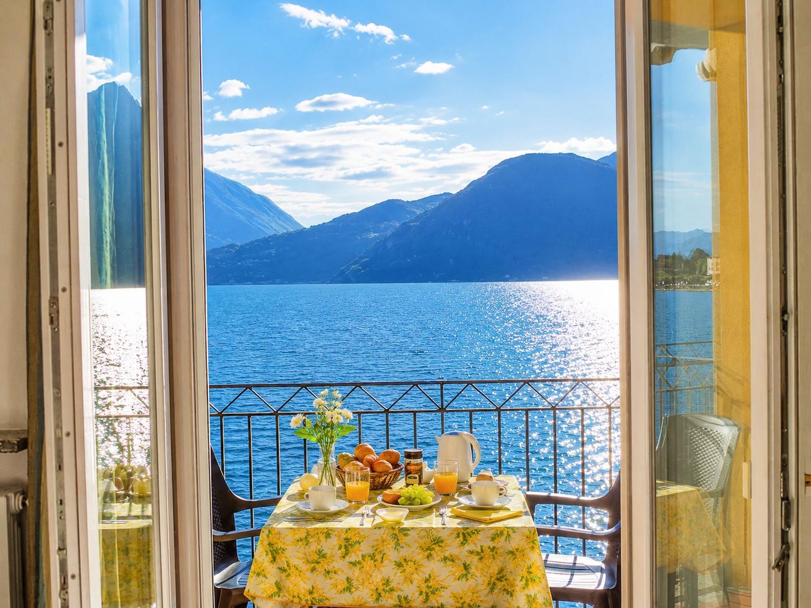 Balkon mit Tisch, Frühstück und Blick auf See und Berge.