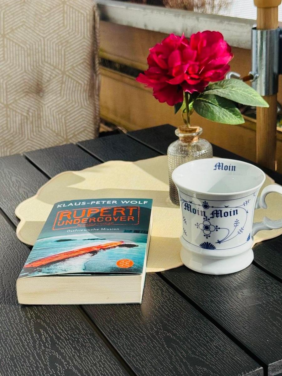 On the table is a cup, a book, and a flower in a glass.