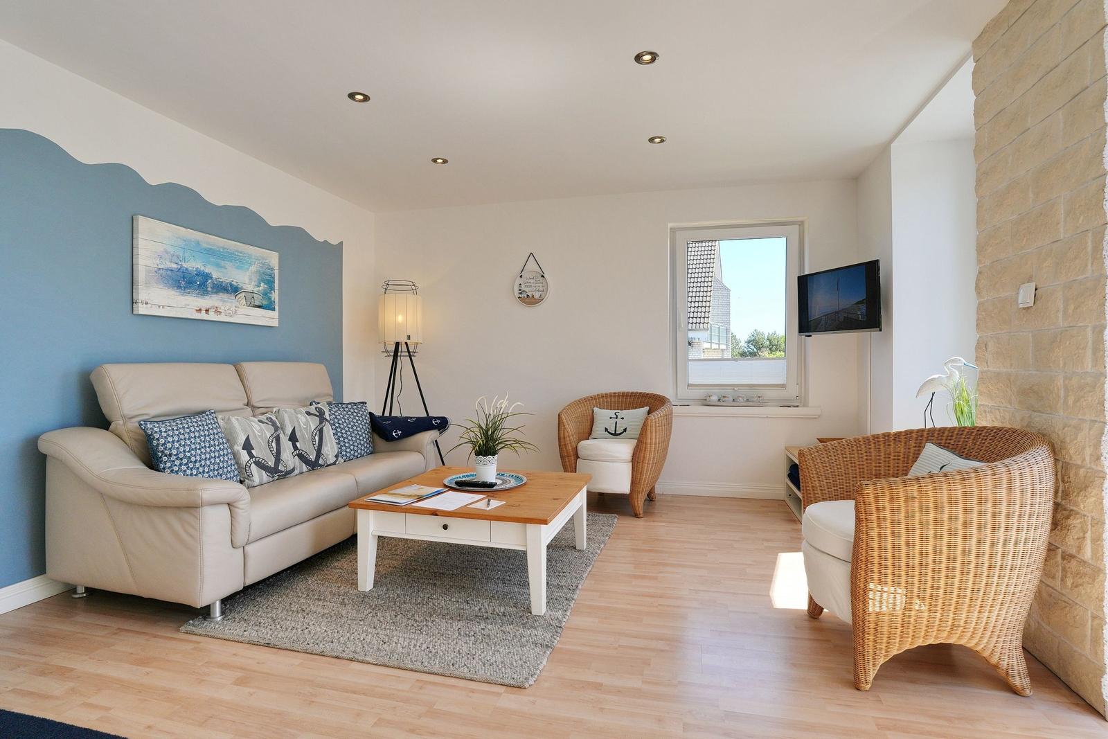 Wohnzimmer mit Sofa, Wickerstühlen und Holzboden. Wand mit blauer Farbe und Seemotiv.