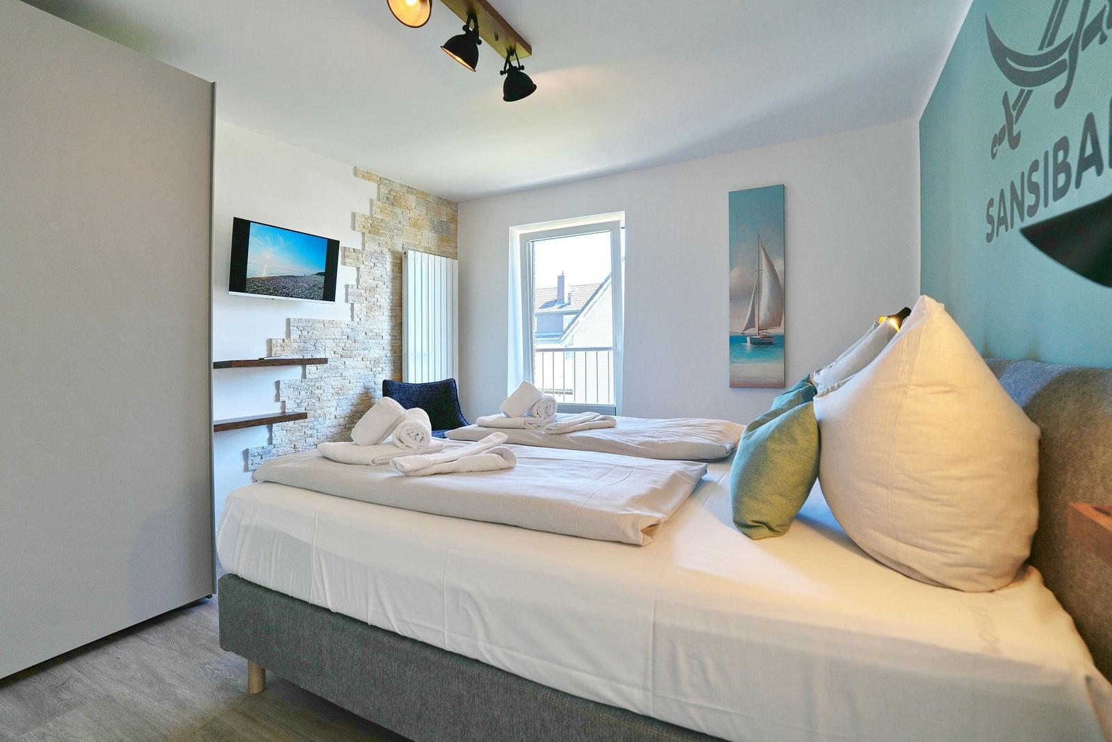 Schlafzimmer mit Doppelbett, Fernseher und Fenster zum Balkon.
