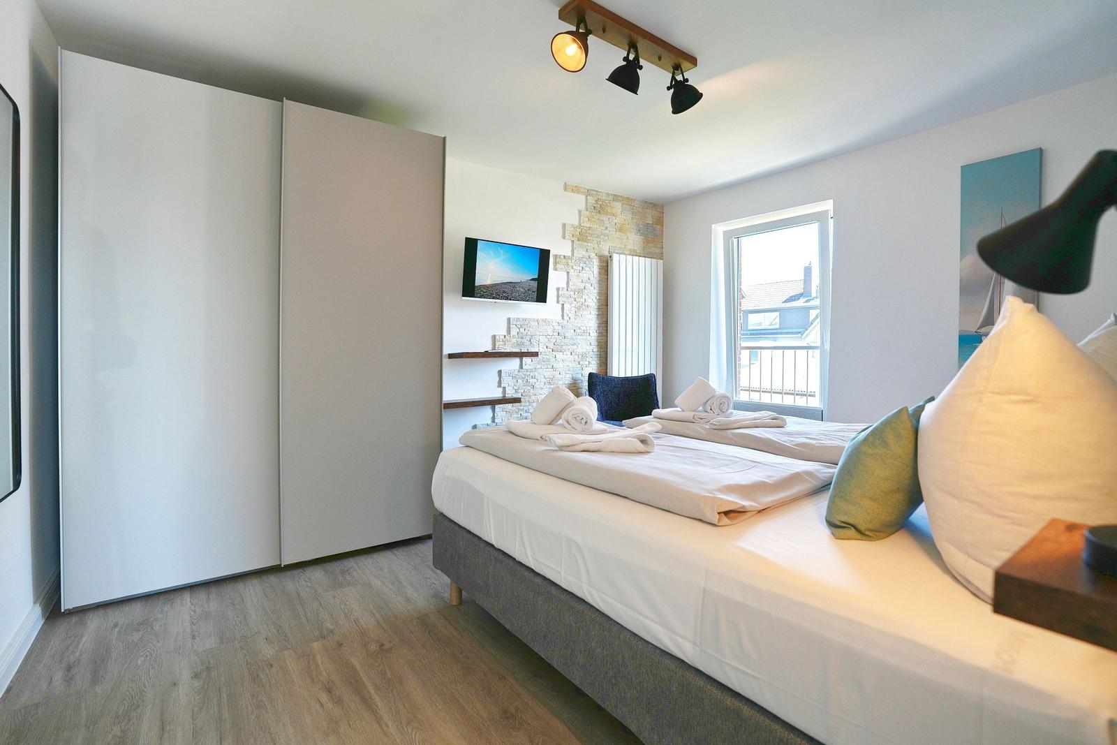 Schlafzimmer mit Doppelbett, Kleiderschrank und Fenster zum Balkon.