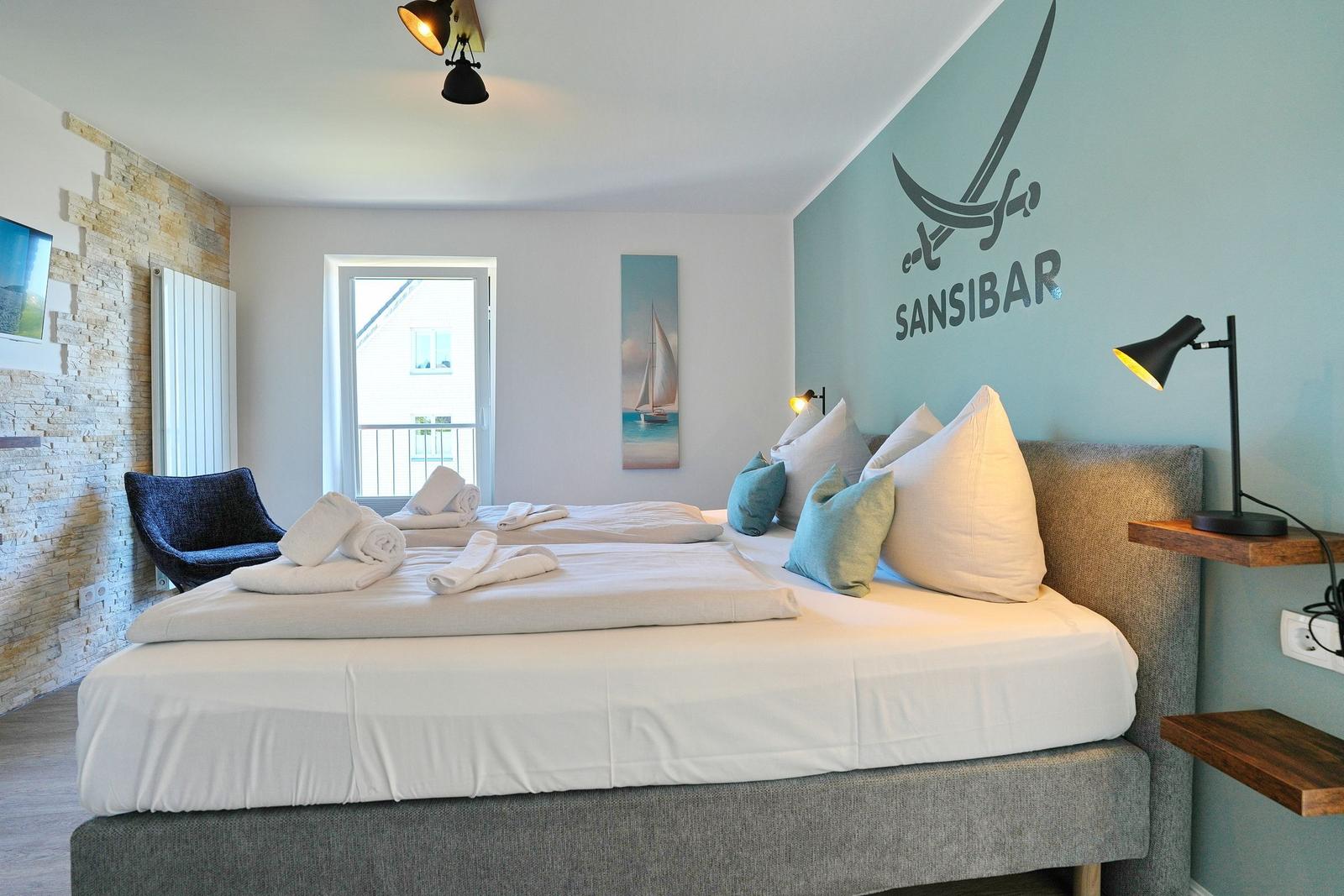 Schlafzimmer mit Bett, Wanddekoration und Blick auf Balkon.
