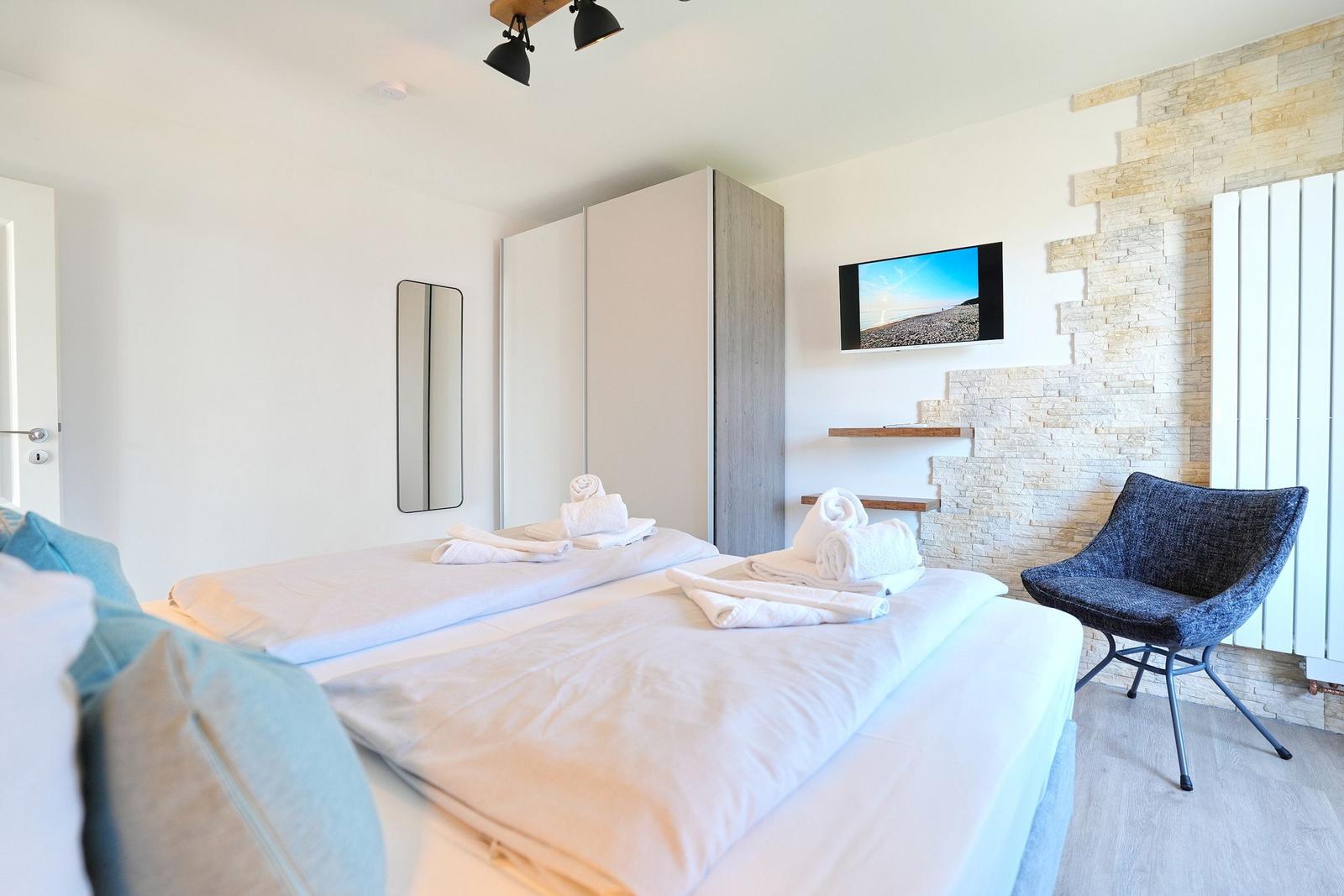 Schlafzimmer mit Doppelbett, TV, Stuhl und Kleiderschrank.