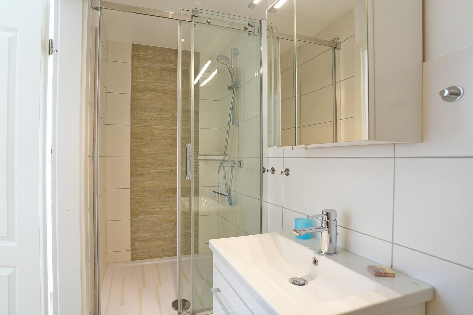 Badezimmer mit Dusche, Waschbecken und Spiegelschrank.