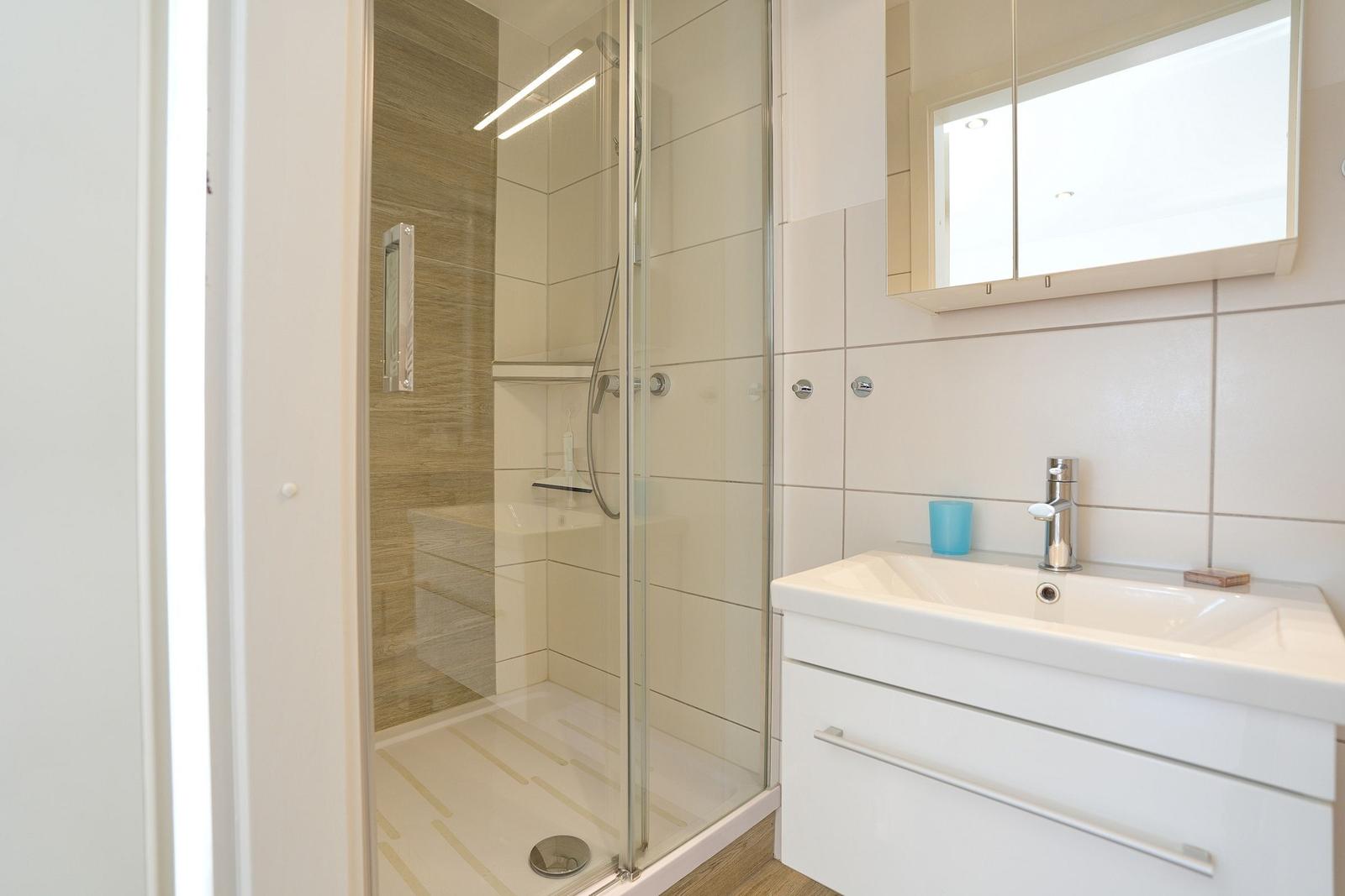 Badezimmer mit Dusche und Waschbecken mit Spiegelschrank.