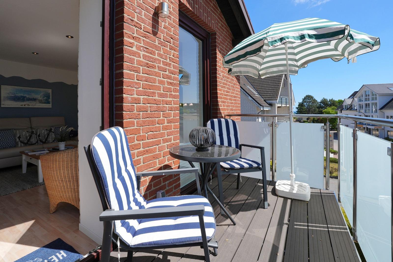 Terrasse mit zwei gestreiften Stühlen, Tisch und Sonnenschirm. Blick auf Wohnbereich und Nachbarhäuser.