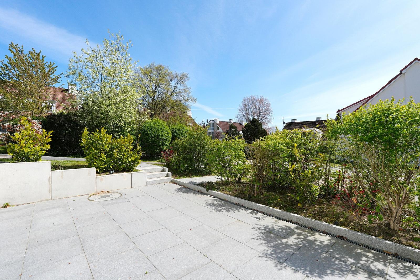 Garten mit gepflastertem Bereich und Bäumen unter blauem Himmel.