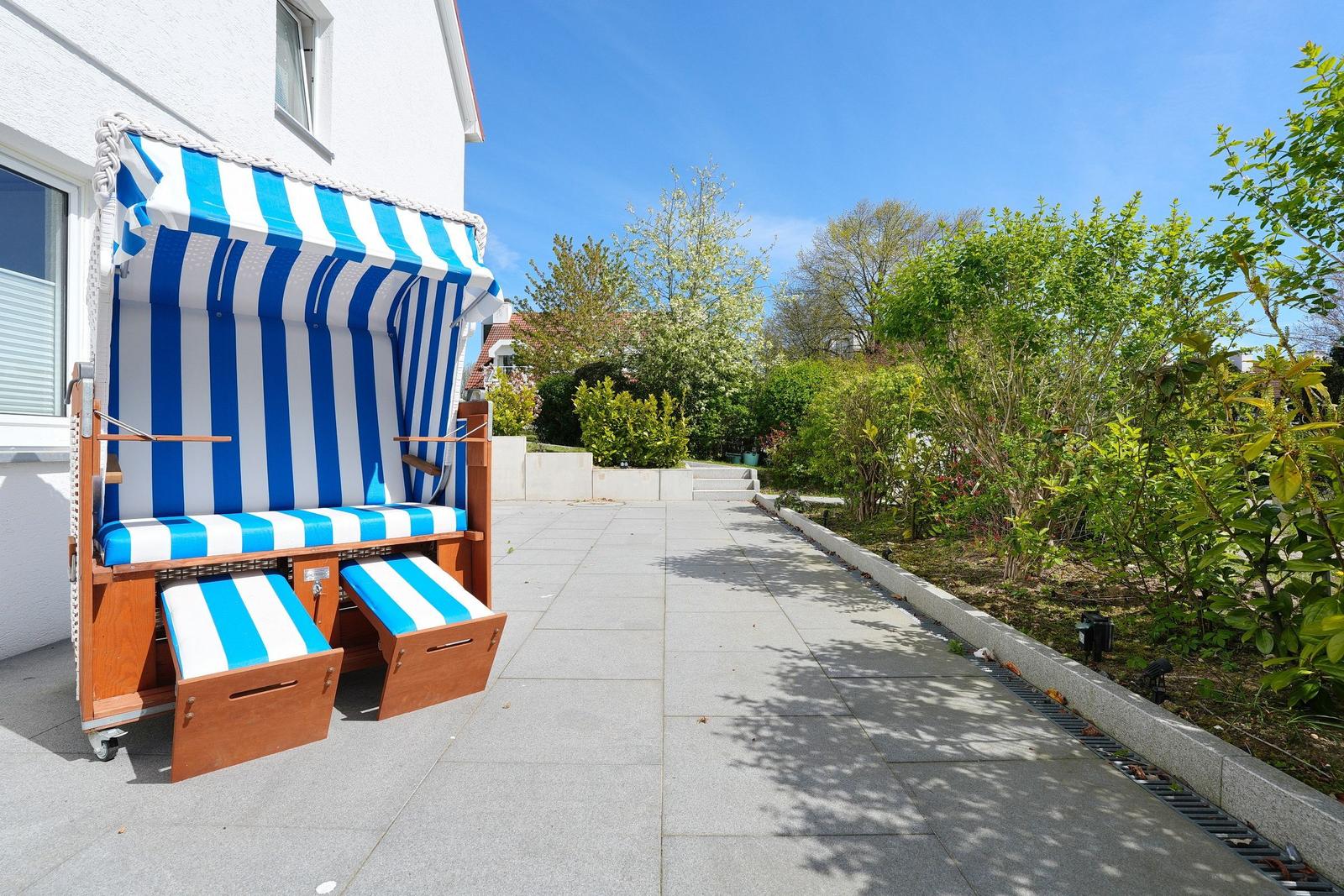 Ein blau-weiß gestreifter Strandkorb steht auf einer Terrasse neben einem Haus.