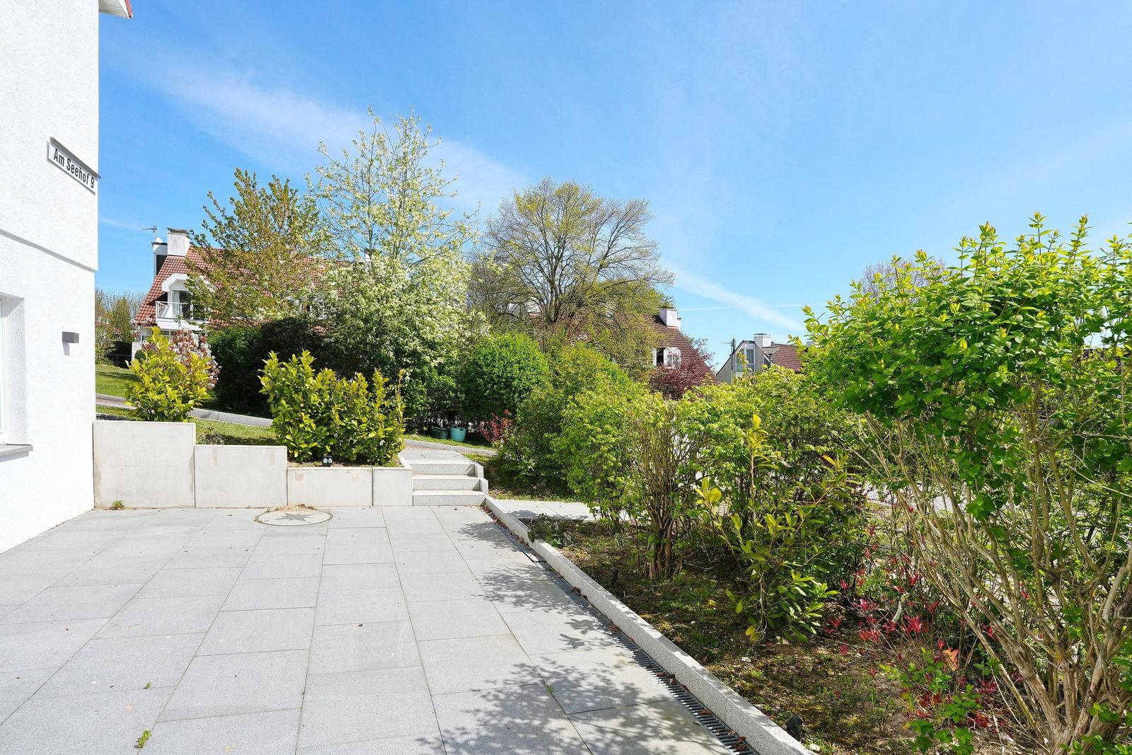 Gartenweg mit Beeten, Bäumen und einem weißen Gebäude. Straßenschild: Am Seehof 9.