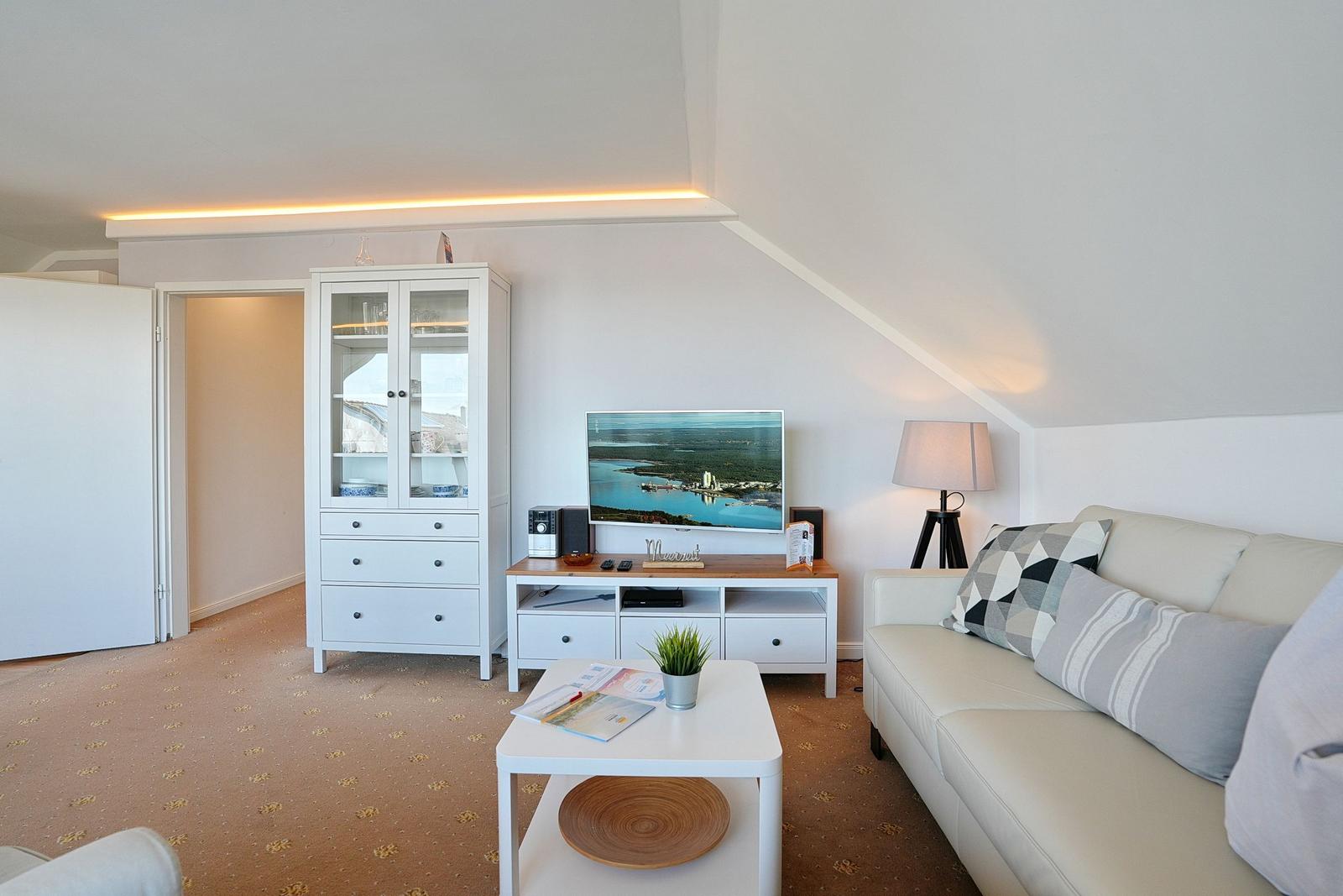 Wohnzimmer mit Sofa, Fernseher und Schrank unter schrägem Dach.