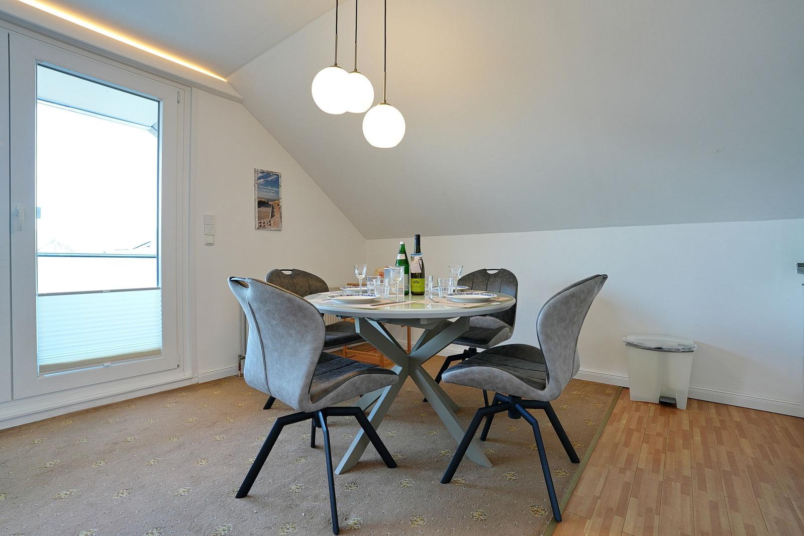 Esszimmer mit runder Tisch, vier Stühlen und großem Fenster. Drei Pendelleuchten hängen über dem Tisch.
