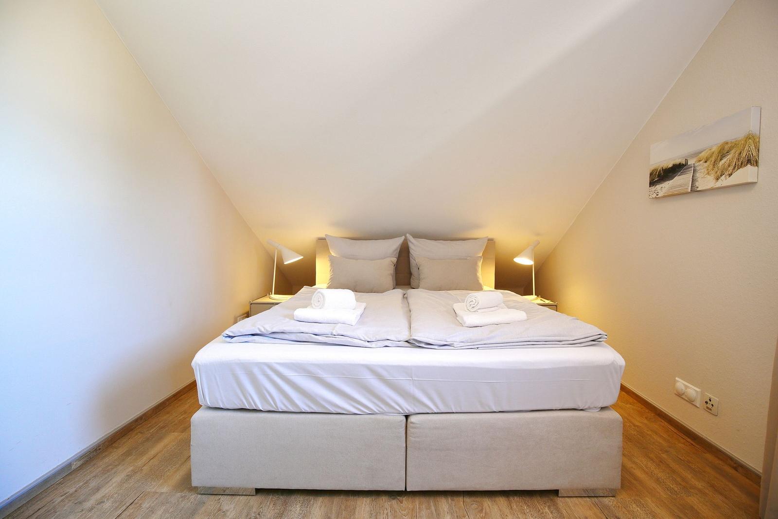 Schlafzimmer mit Doppelbett, Holzboden und Dachschrägen. Zwei Nachttische mit Lampen.
