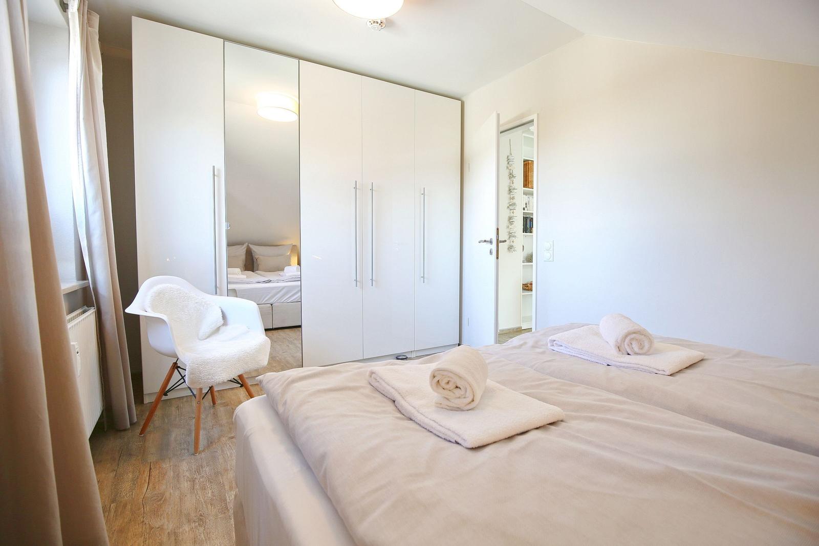 Zimmer mit Doppelbett, weißem Schrank und Stuhl. Handtuch auf dem Bett.