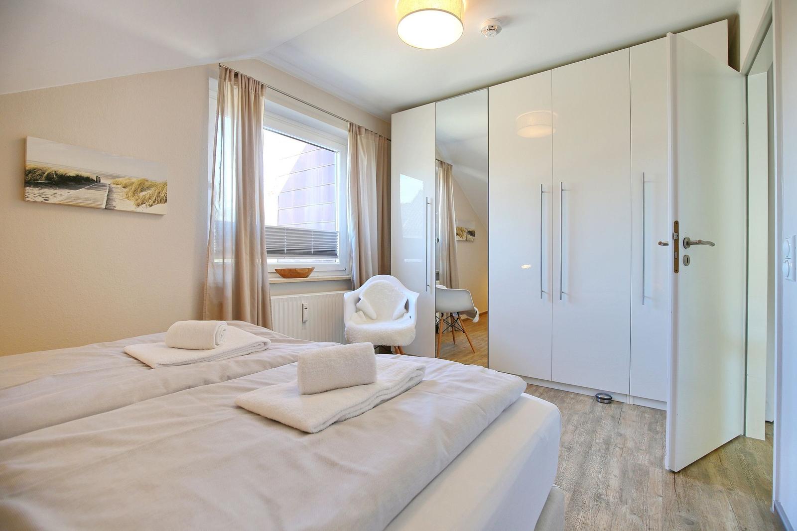Schlafzimmer mit Doppelbett, weißen Schränken und Fenster mit Vorhängen.