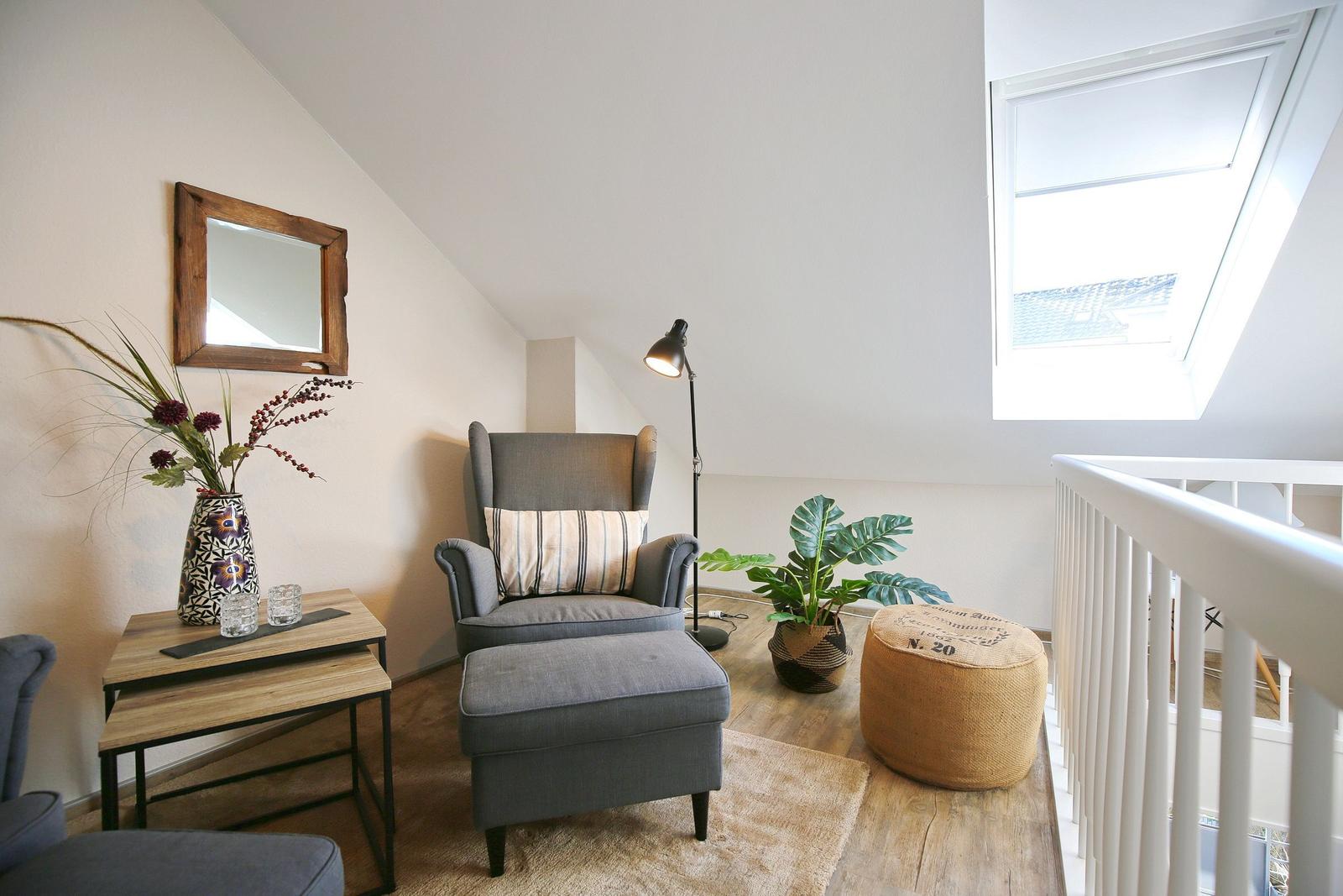 Ein Schlafzimmer mit Sessel, Pflanzen und Fenster. Holzfußboden und Wandspiegel.