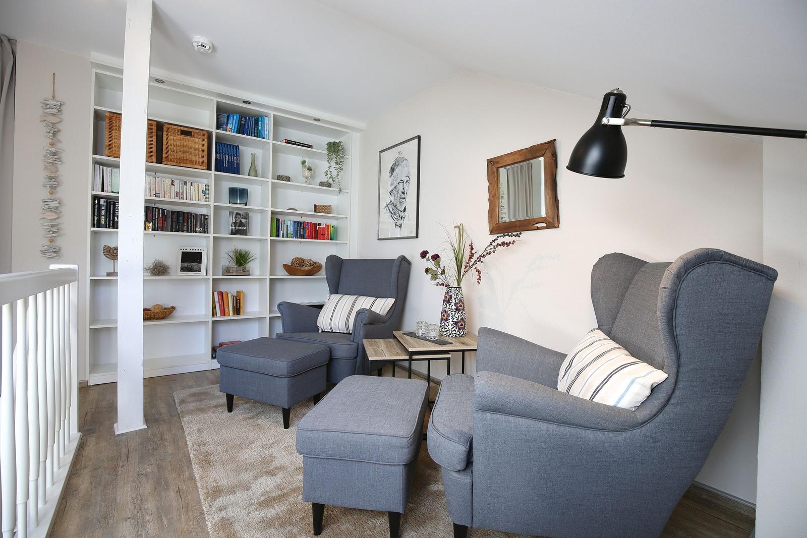 Zwei graue Sessel mit Fußhocker, Bücherregal und Wandspiegel im Wohnbereich.