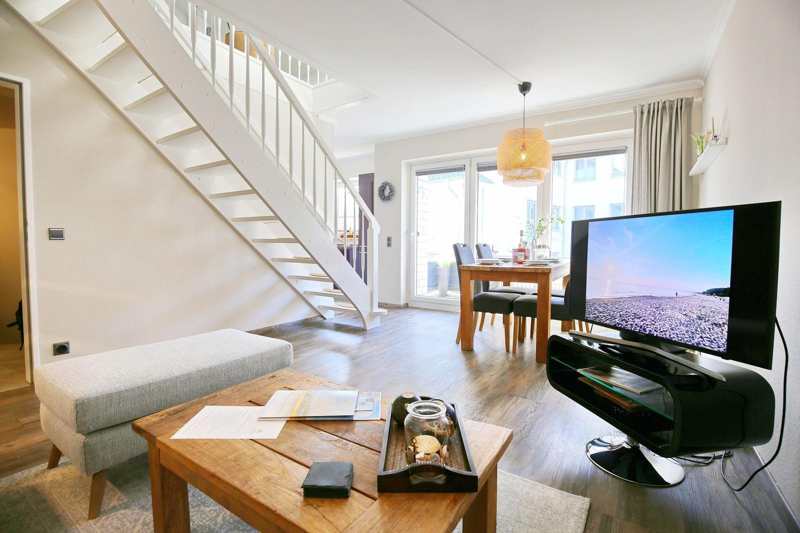 Wohn- und Essbereich mit TV, Tisch und Stühlen, Holzboden und Treppe.