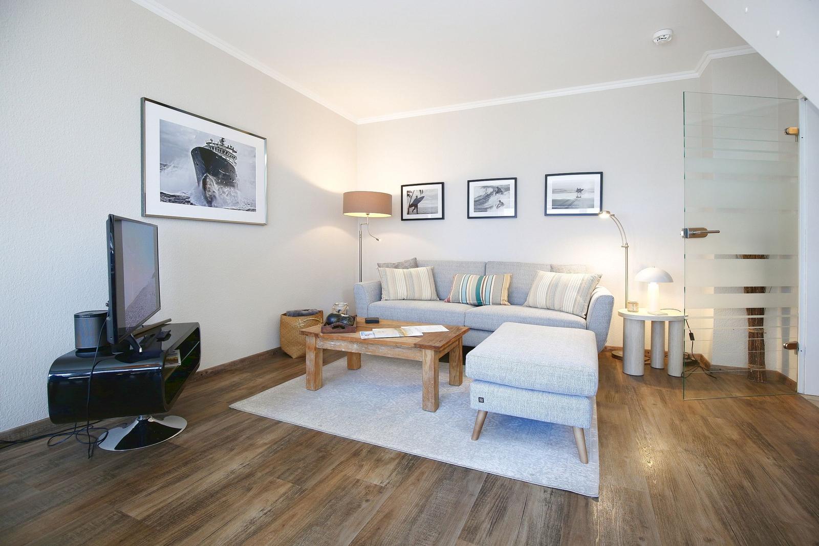 Wohnzimmer mit Sofa, Couchtisch und Fernseher. Glaswand trennt Raum.