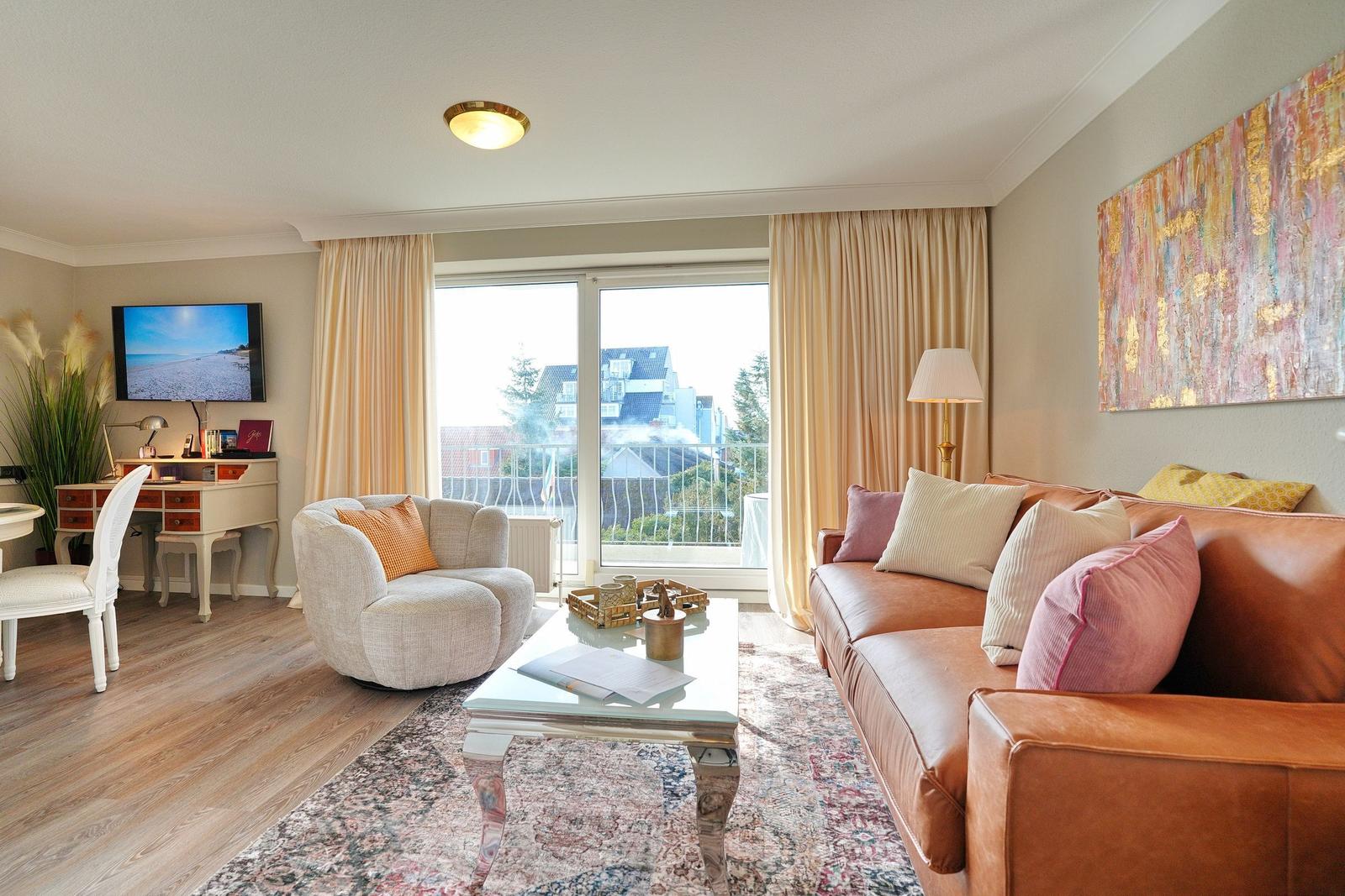 Wohnzimmer mit Sofa, Sessel und TV. Blick auf Balkon mit Stadtaussicht.