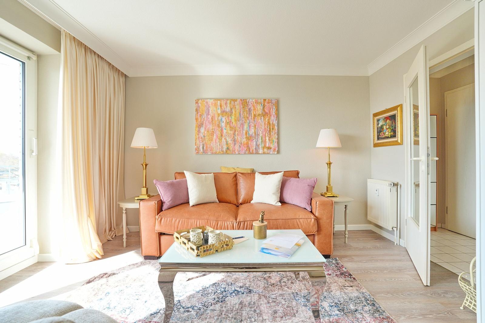 Ein Wohnzimmer mit einem orangefarbenen Sofa, einem Glas-Tisch und einem großen Wandbild.