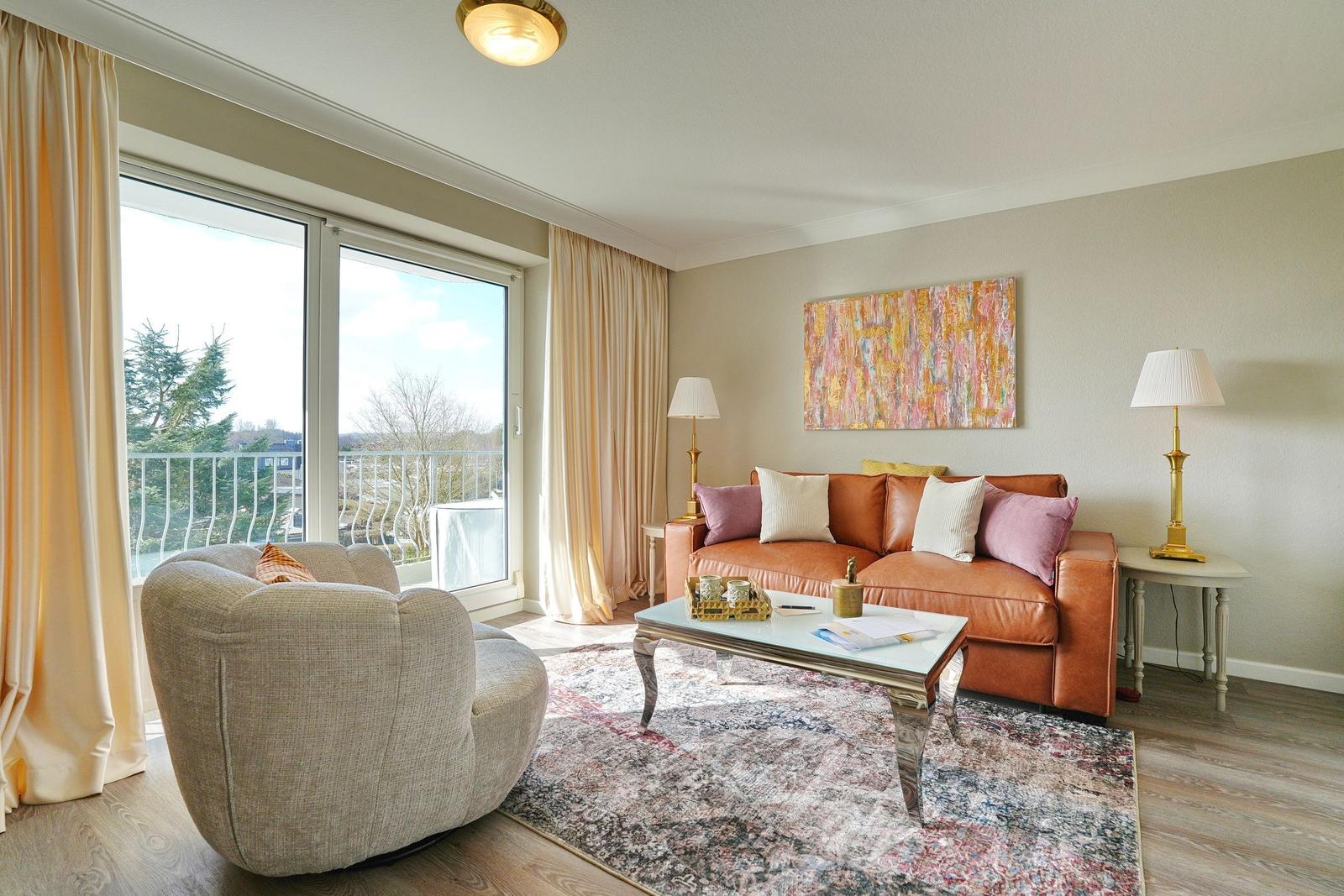 Ein Wohnzimmer mit braunem Sofa, Beistelltischen und einem großen Fenster mit Blick auf Balkon.