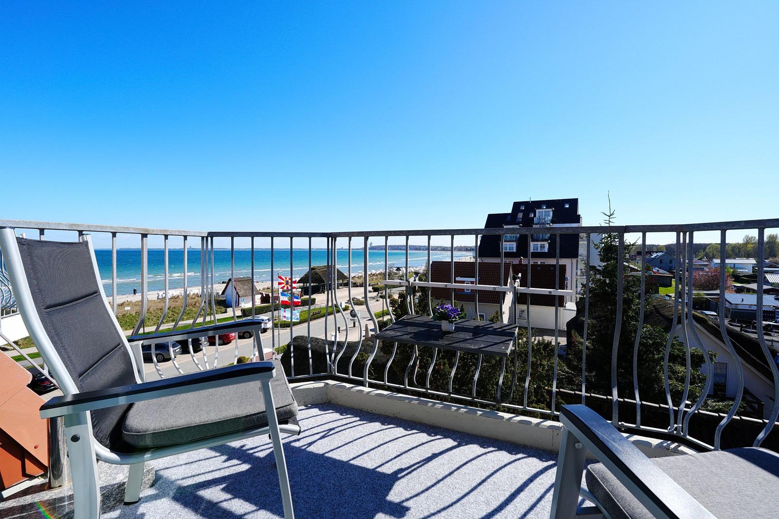 Terrasse mit Sitzgelegenheiten und Meerblick. Hintergrund: Strand und Gebäude.