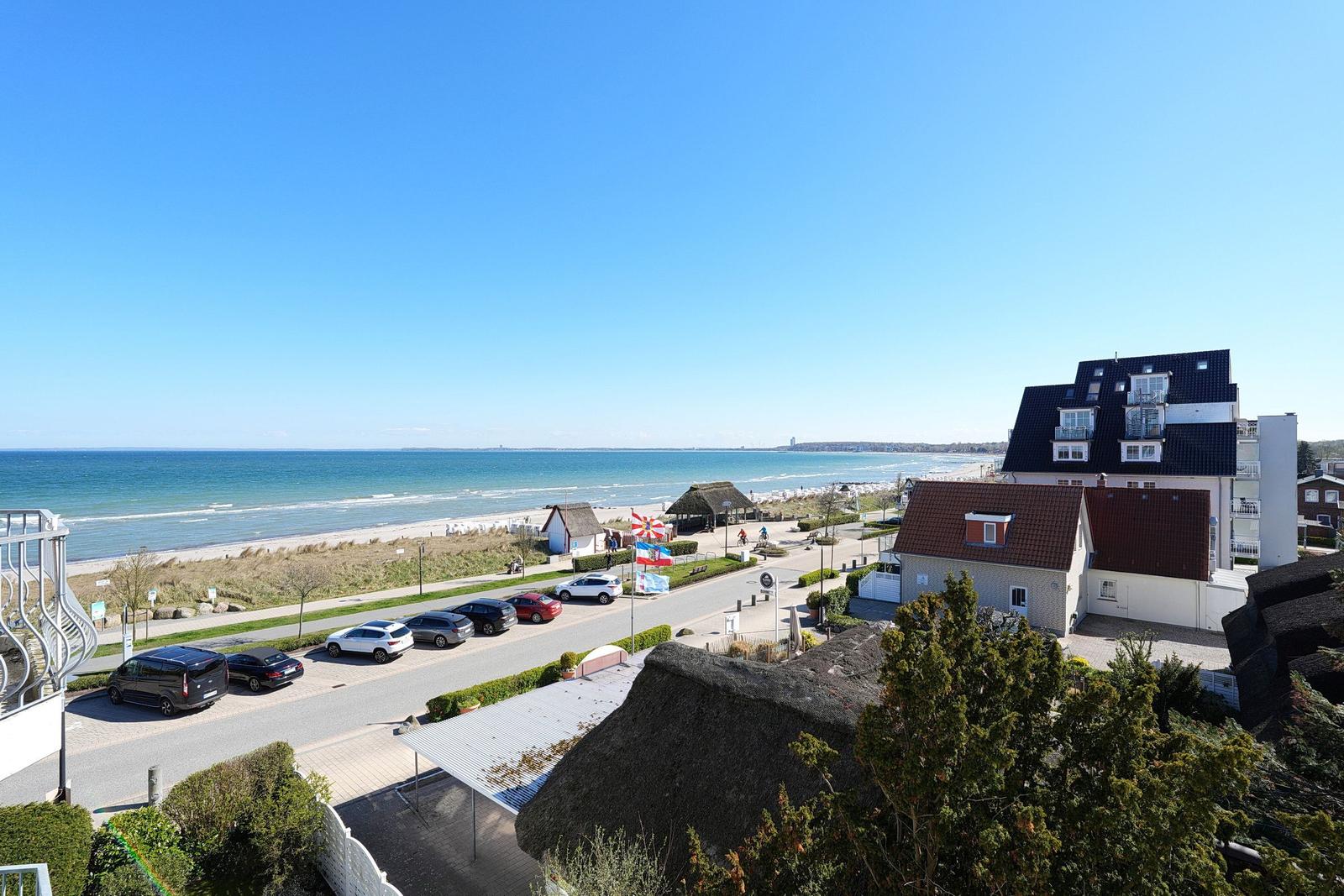 Meerblick mit Strand, Parkplatz und Häusern in der Ferne.