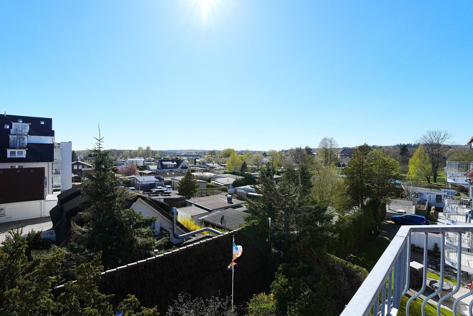 Blick vom Balkon auf Dächer, Bäume und einen klaren Himmel.