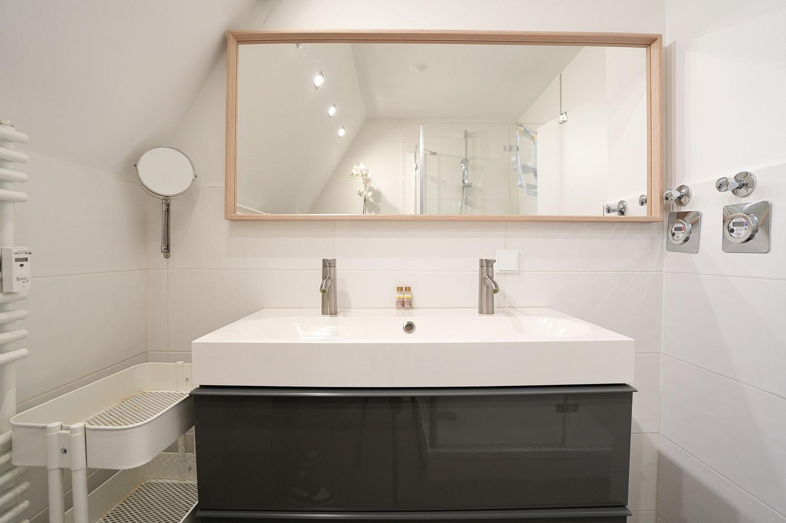 Badezimmer mit Waschbecken, Spiegel und Dusche.