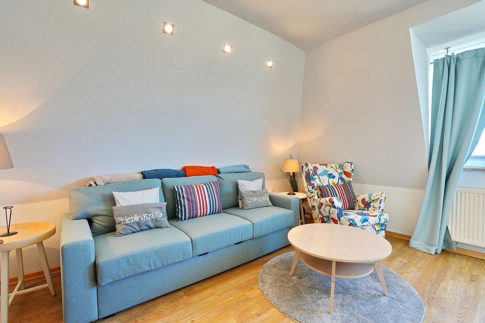 Ein Wohnzimmer mit einem hellblauen Sofa, einem gemusterten Sessel und einem runden Tisch.