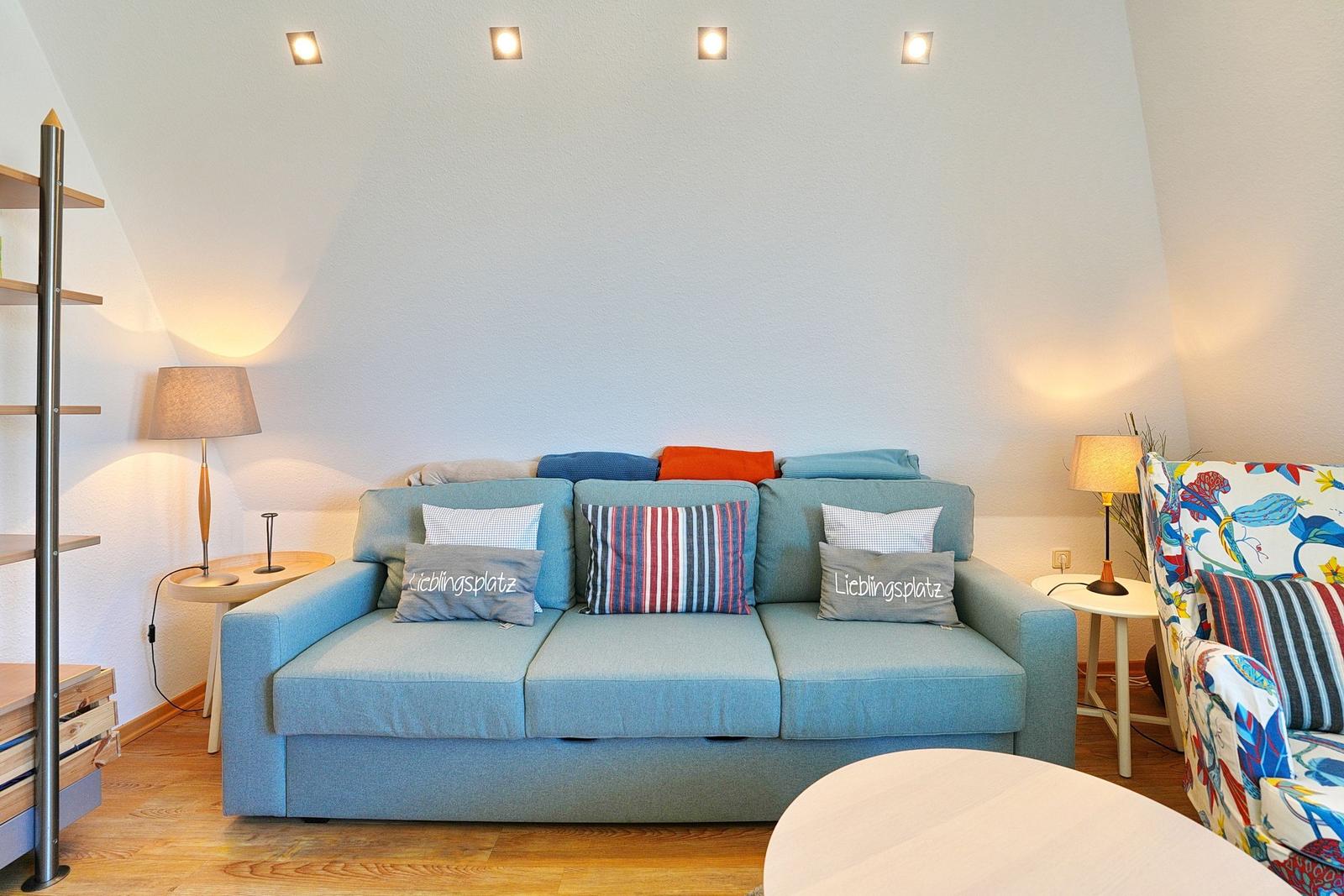 Ein Wohnzimmer mit blauem Sofa, dekorativen Kissen und zwei Stehlampen.