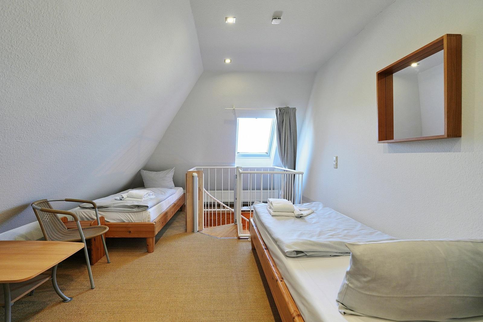 Zimmer mit zwei Betten, Tisch, Stuhl und Fenster. An der Wand hängt ein Spiegel.