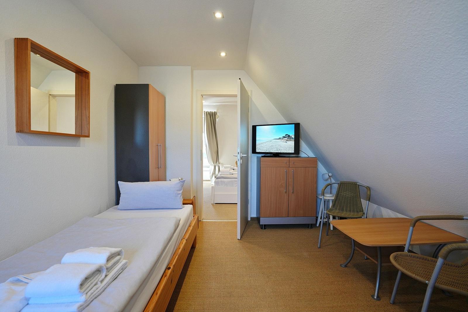 Ein Schlafzimmer mit Bett, Fernseher und Tisch. Durchgang zur nächsten Wohnung.
