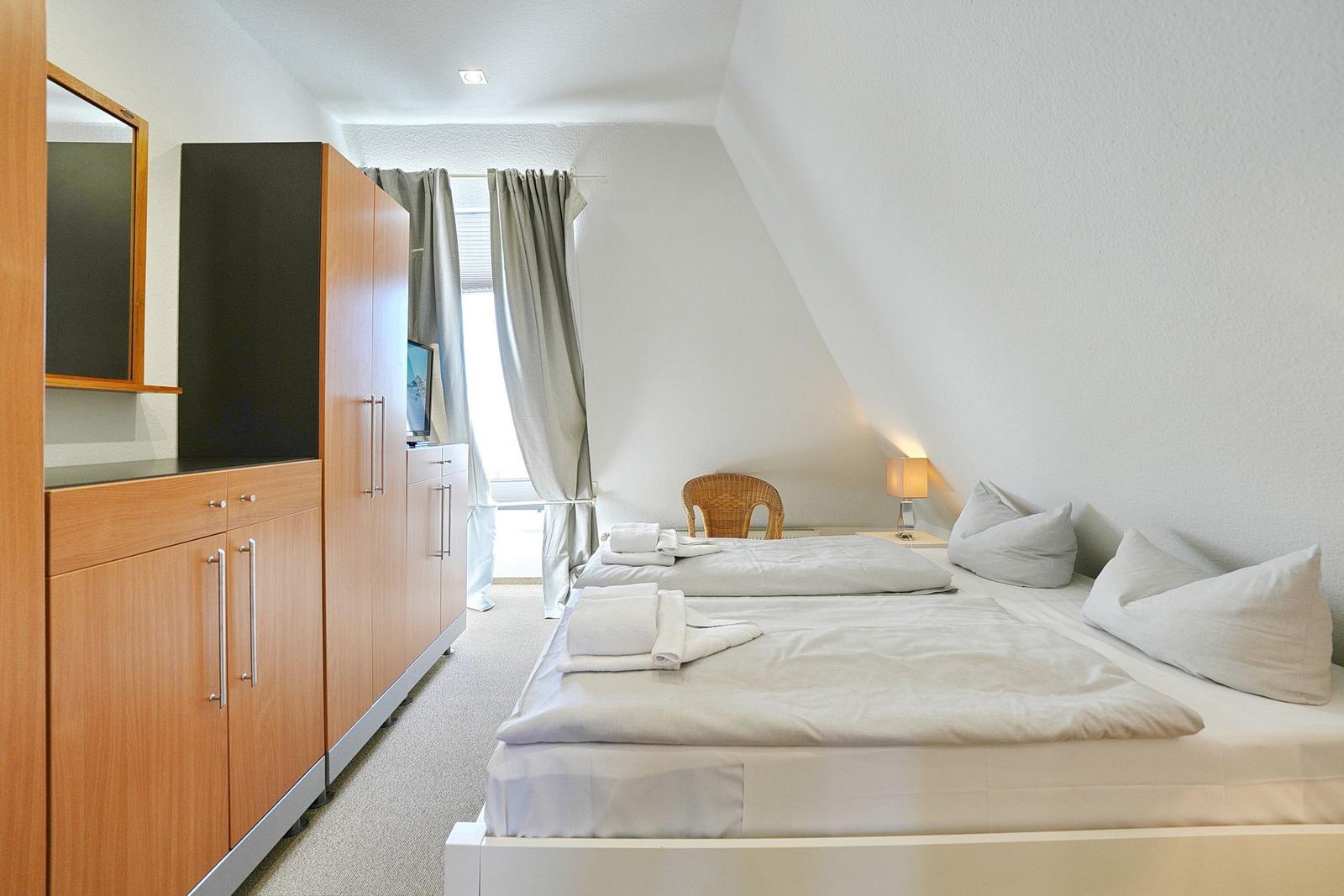 Schlafzimmer mit Doppelbett, Kleiderschrank und Fenster mit Vorhängen.