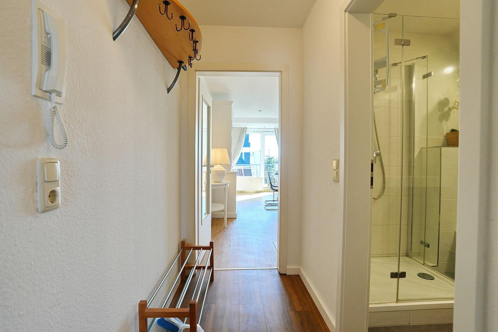 Flur mit Dusche, Garderobe und Blick in Wohnbereich mit Balkon.