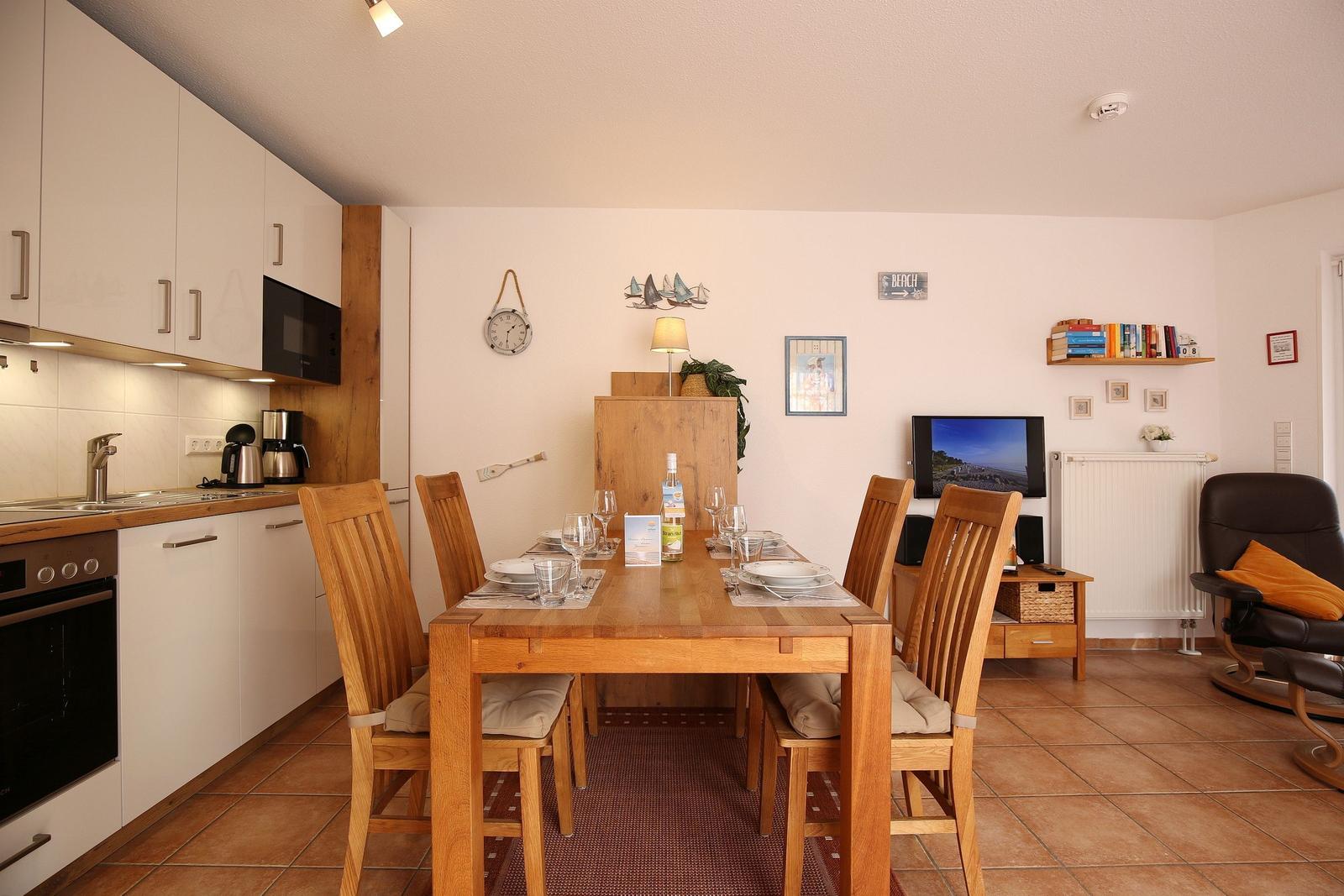 Essbereich mit Holztisch, Stühlen und Küchenzeile im Hintergrund.