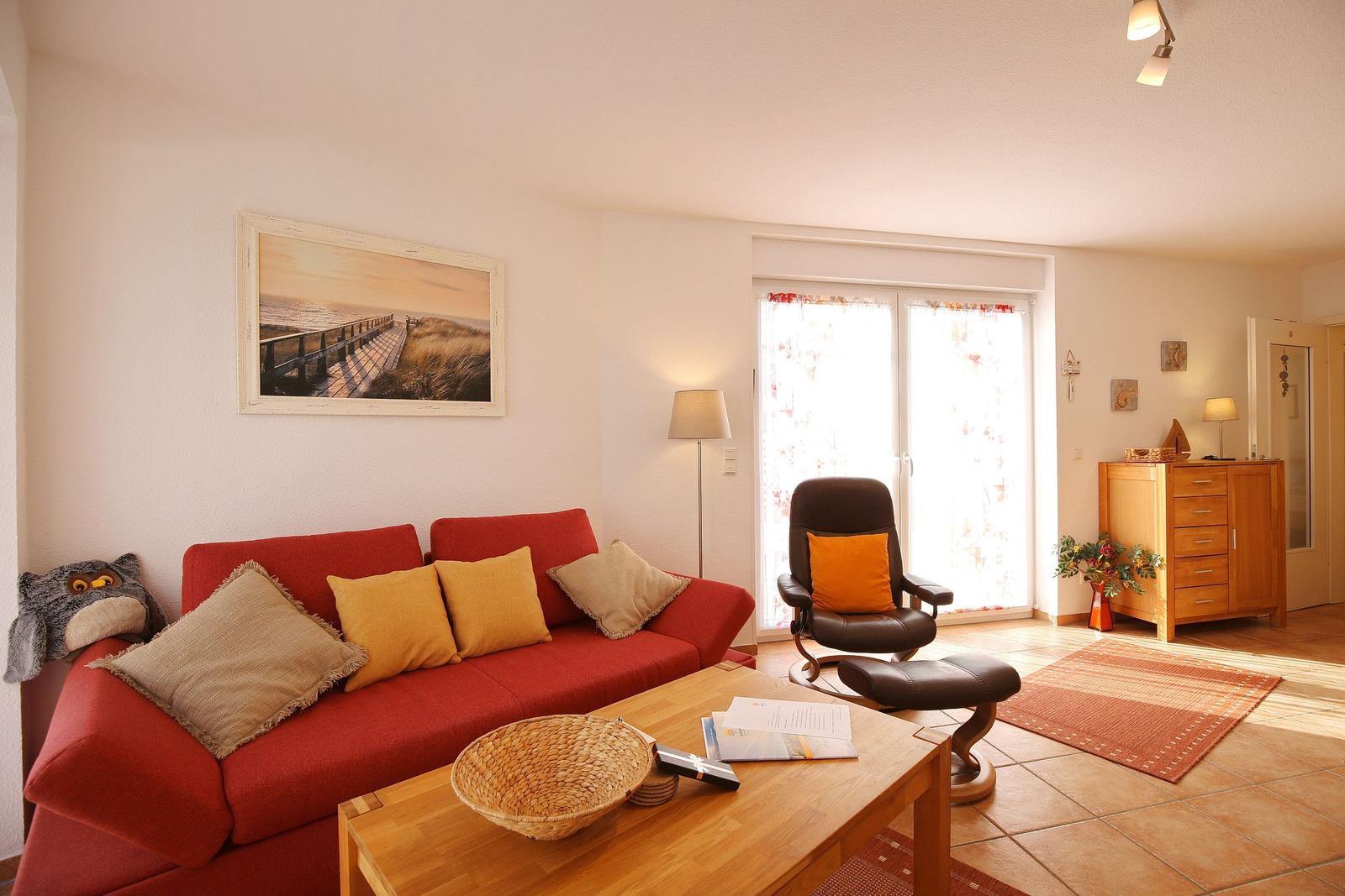 Ein Wohnzimmer mit rotem Sofa, Holztisch und Sessel vor Fenster.