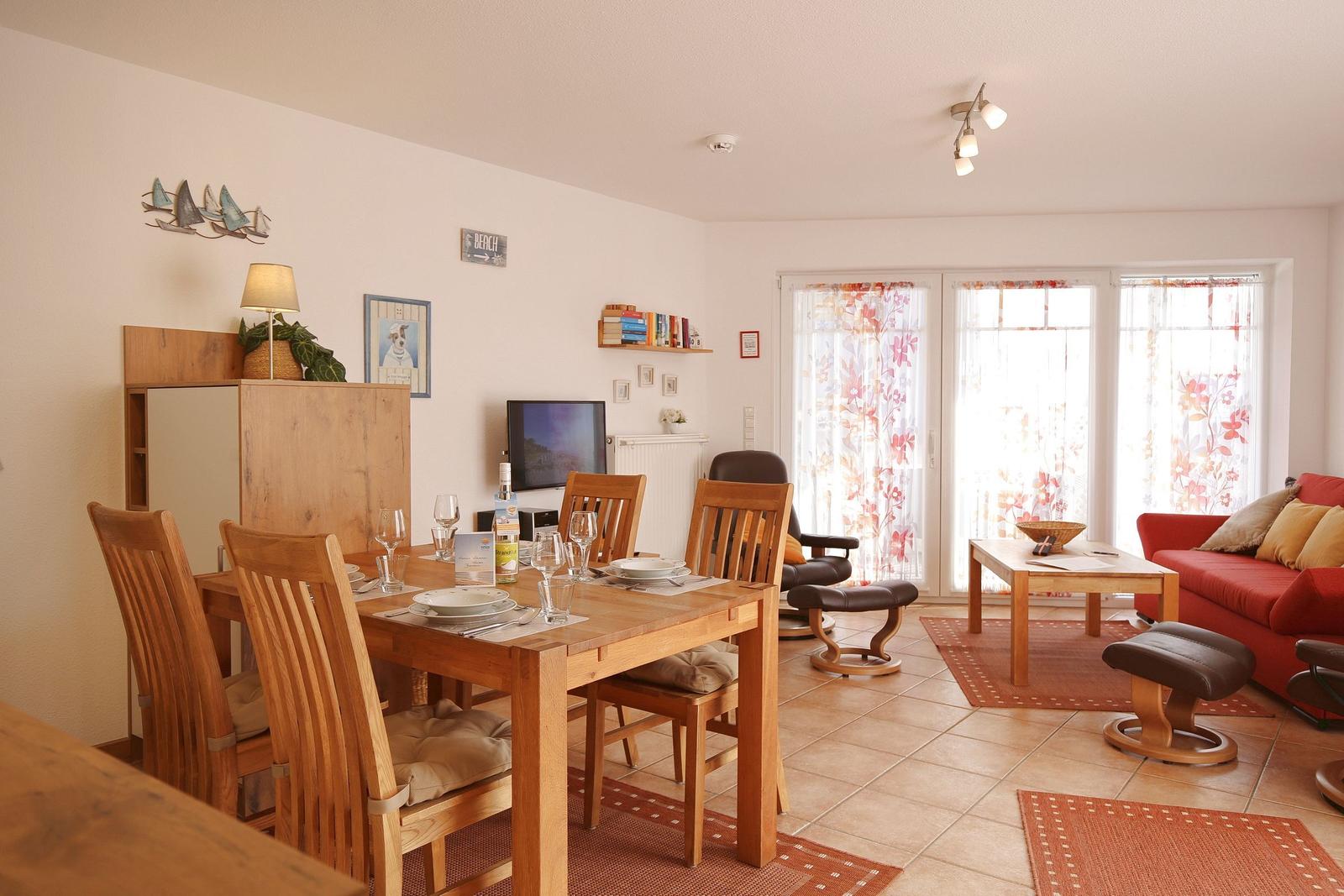 Essbereich mit Holztisch und Stühlen, Wohnbereich mit rotem Sofa und Fenster mit floralen Vorhängen.