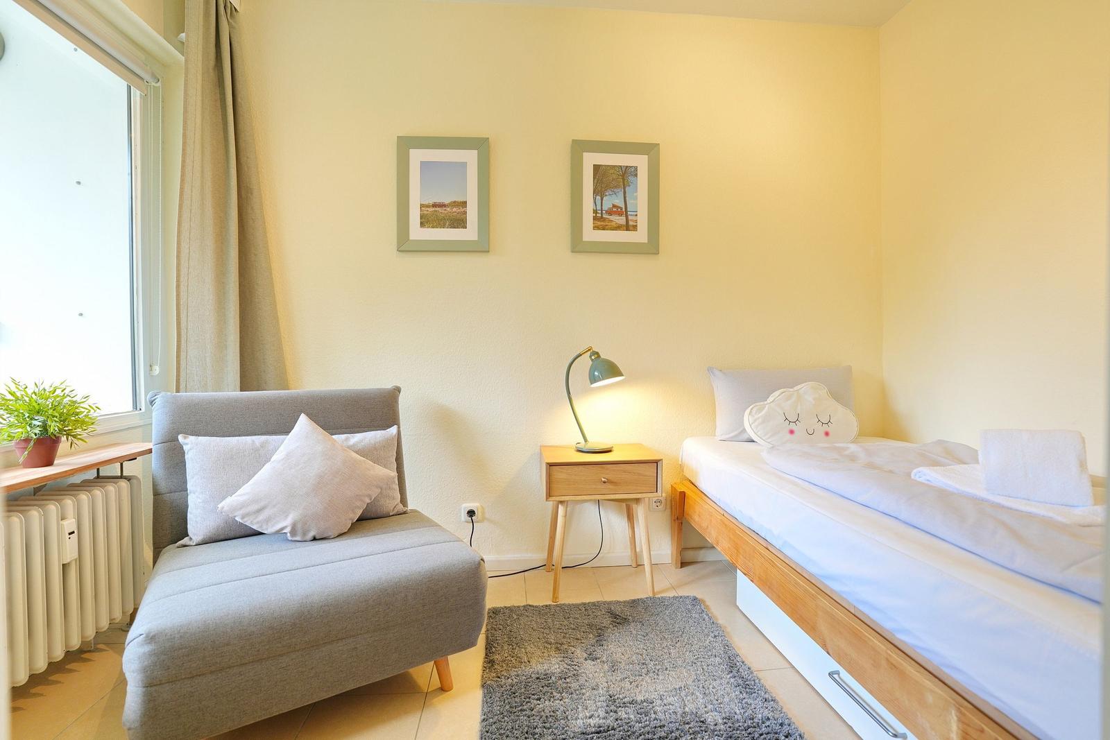 Ein Schlafzimmer mit einem Bett, einem Sessel und einem Nachttisch mit Lampe.