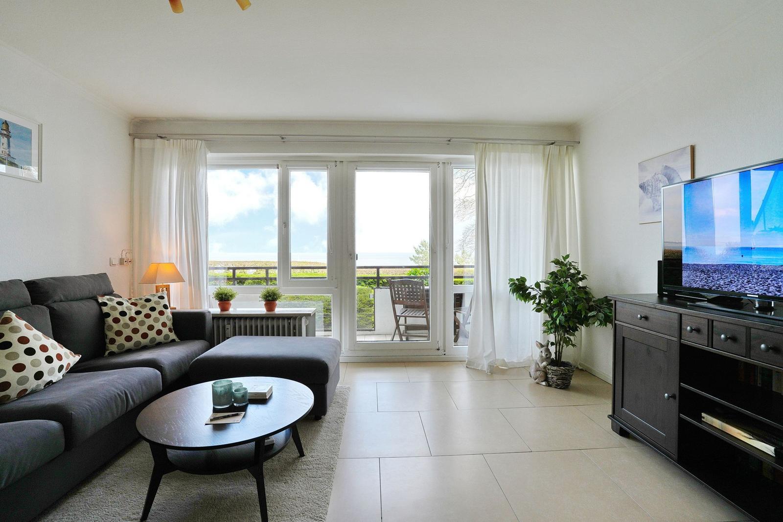 Wohnzimmer mit Sofa, Couchtisch und TV. Balkon mit Meerblick.