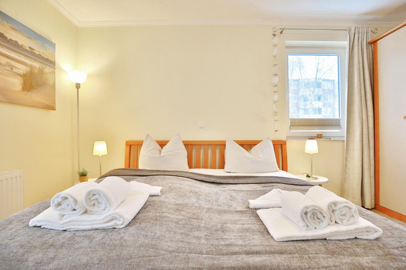 Bedroom with bed, nightstands, and window. Towels are neatly placed on the bed.