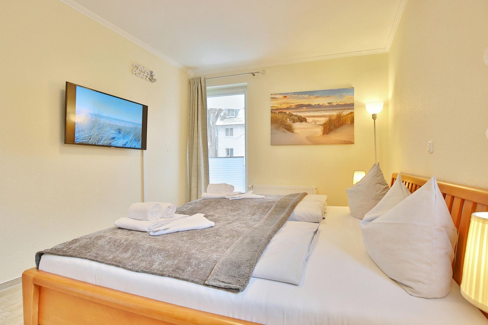 Bedroom with bed, TV, and window. Wall art and floor lamp.